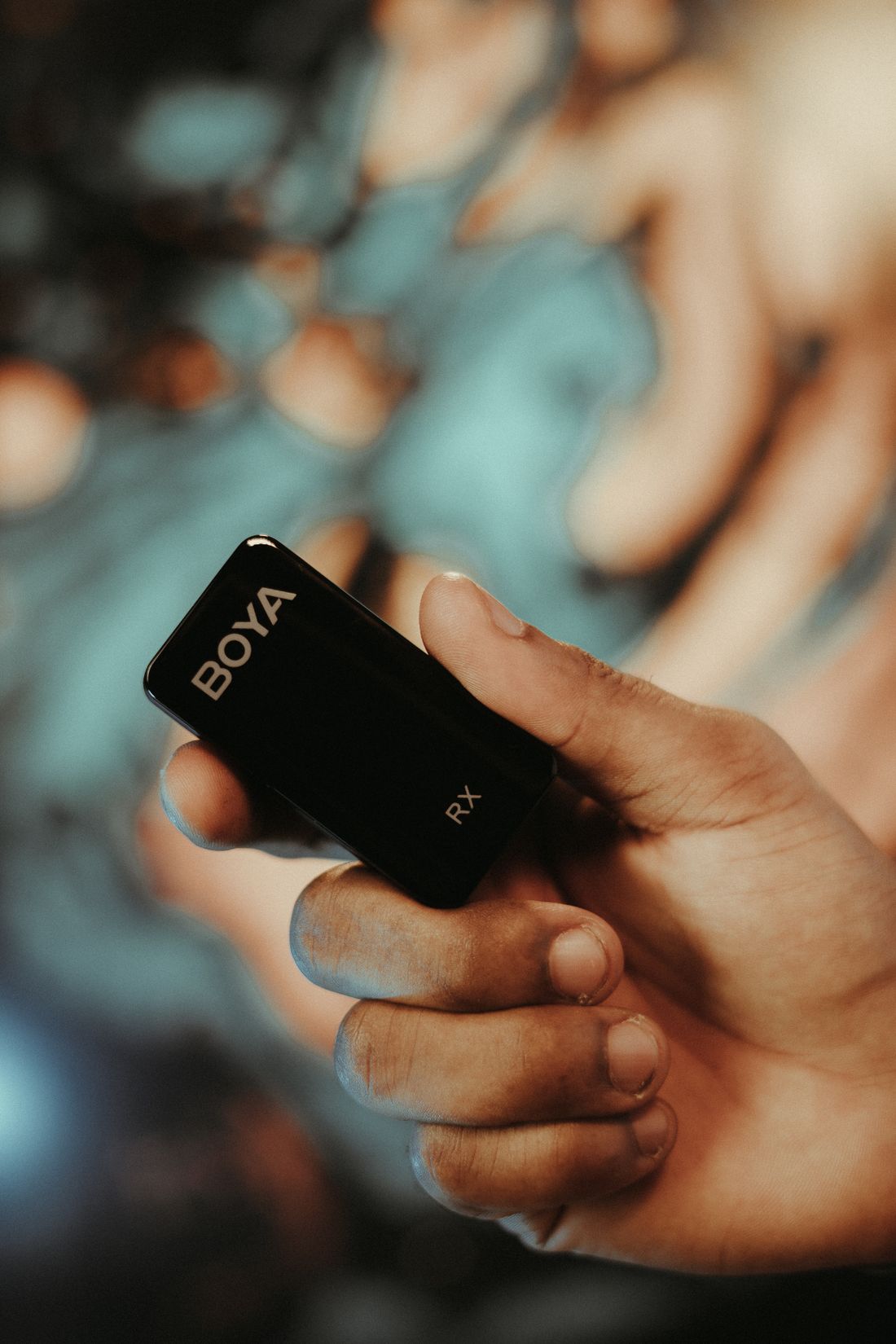 A hand holding a compact wireless microphone receiver.