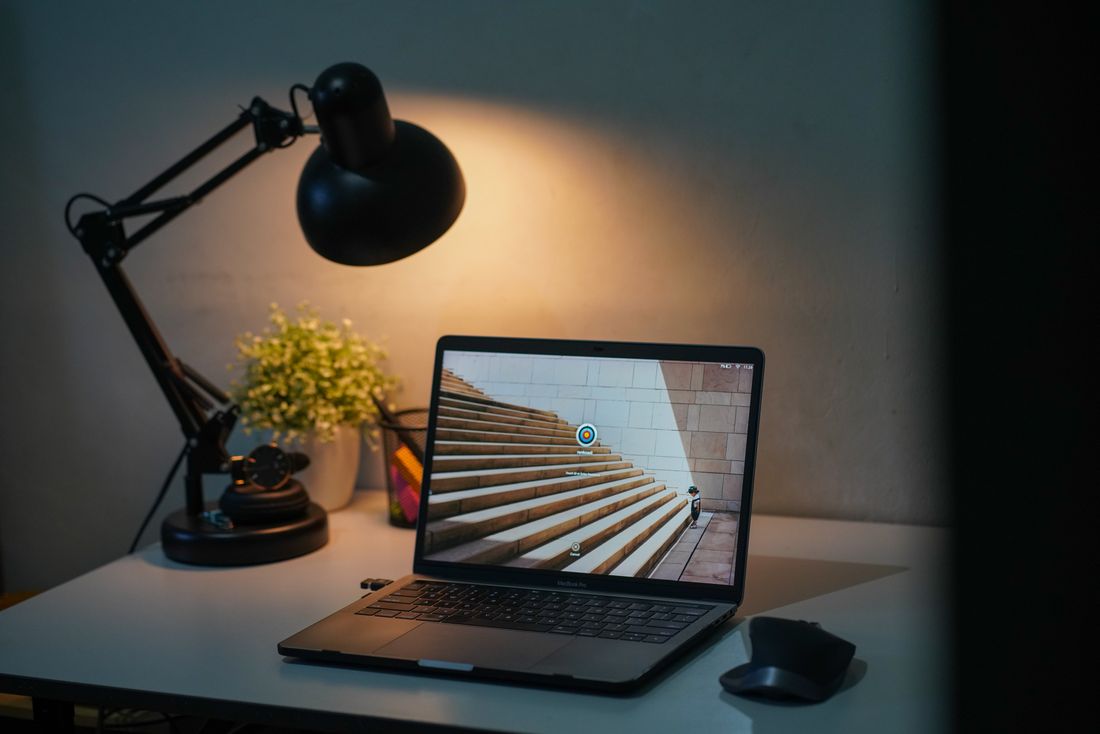 A simple home desk with laptop, lamp and potted plant.